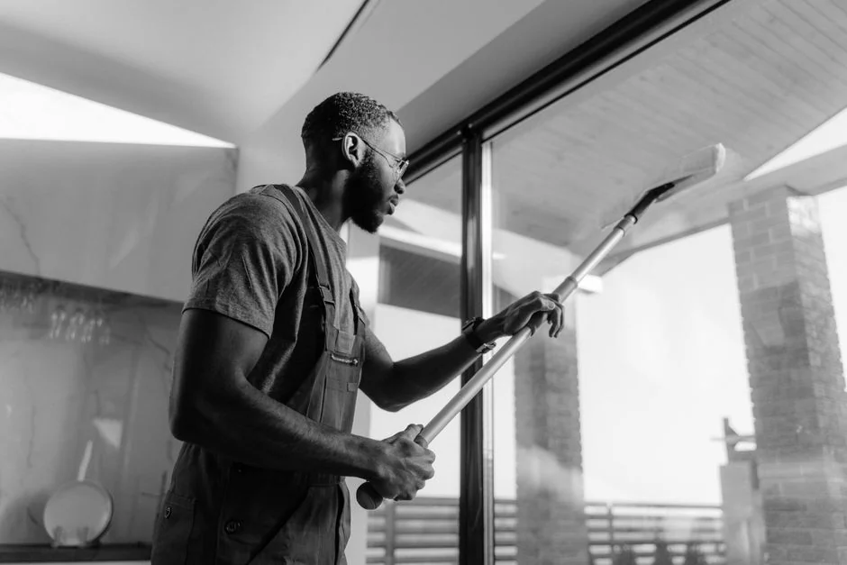 A man cleaning a glass door indoors using a spray bottle and cloth.